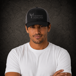A man wearing a black and gray Phoenix Redline trucker hat and a white t-shirt, standing against a dark textured background.
